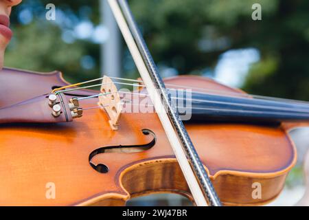 Nahaufnahme des Violinbogens auf Streichern, die von einer unerkennbaren Frau im Freien gespielt werden. Stockfoto