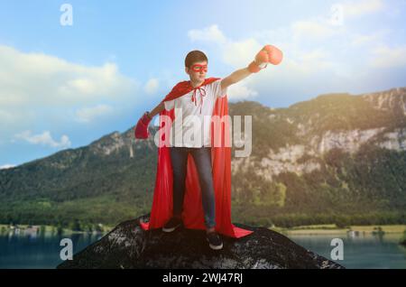 Superheld, Motivation und Kraft. Junge im cape und Maske mit Boxhandschuhen auf der hohen Spitze in den Bergen Stockfoto