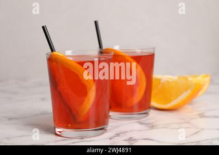 Aperol Spritz Cocktail, Orangenscheiben und Strohhalme in Gläsern auf weißem Marmortisch Stockfoto