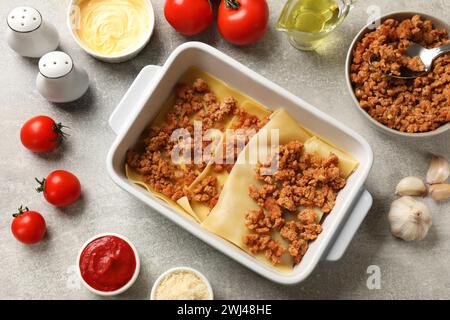 Lasagne kochen. Pasta-Blätter, Hackfleisch in Backblech und Produkte auf einem hellen, strukturierten Tisch, flach liegend Stockfoto