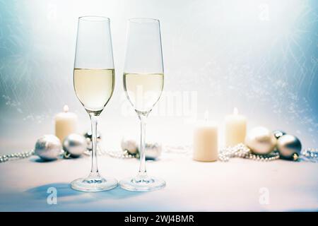 Zwei Sektflötengläser, Kerzen und festliche Weihnachtsdekoration auf blaugrauem Hintergrund mit hellem Party-Bokeh für Stockfoto