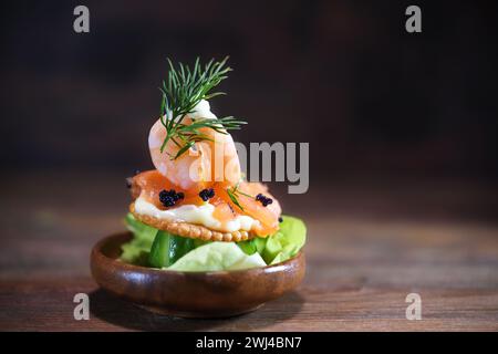 Garnelen, Lachs und Kaviar auf einem Cracker mit Mayonnaise in einer kleinen Holzschale auf einem dunklen rustikalen Hintergrund, Snack für einen Urlaub p Stockfoto