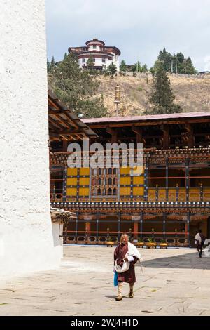 Ein Regierungsangestellter in Paro Dzong mit dem Ta Dzong (Wachturm) oben. Stockfoto
