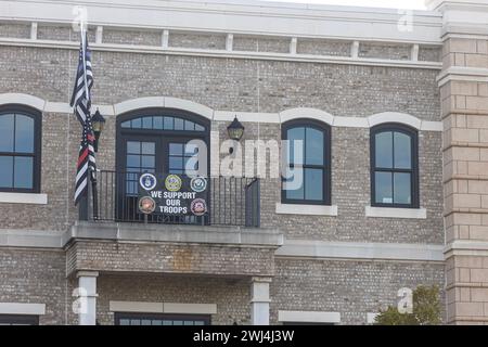 Suwanee, GA / USA - 4. August 2023: Ein Banner mit der Aufschrift 'Wir unterstützen unsere Truppen' und Feuerwehrflaggen und Strafverfolgungsflaggen hängen von einem Balkon der Wohnung. Stockfoto