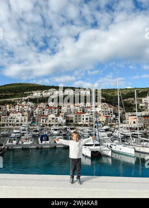 Das kleine Mädchen steht auf dem Pier vor dem Hintergrund von verankerten Yachten Stockfoto