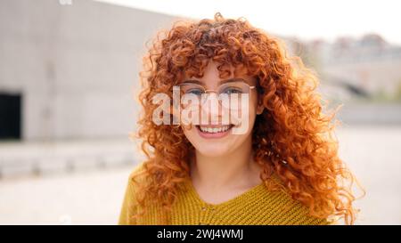 Rothaarige Frau mit lockigen, langen Haaren, die vor der Kamera lächelt Stockfoto
