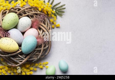 Eine Nahaufnahme der pastellfarbenen Ostereier in einem kleinen Korb, dekoriert mit gelben Frühlingsblumen, symbolisiert die Osterfeier. Stockfoto