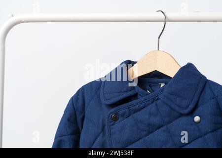 Blauer gesteppter Kindermantel am Aufhänger an der weißen Wand Stockfoto