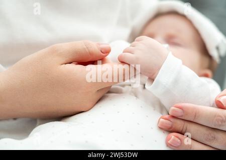 Das Neugeborene findet Trost, den Finger der Mutter während der Krankheit zu halten. Das Konzept des mütterlichen Komforts in der Belastungszeit Stockfoto