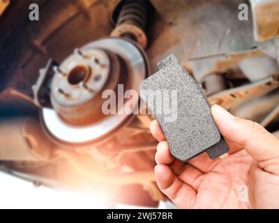 Bremsbeläge in den Händen eines Mechanikers mit unscharfen Bremsscheiben und Bremssätteln auf dem Hintergrund , Autoersatzteile und Wartungskonzept Stockfoto