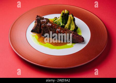 Gebratenes Schweinefleisch mit Sauce und Brokkoli auf rotem Teller Stockfoto