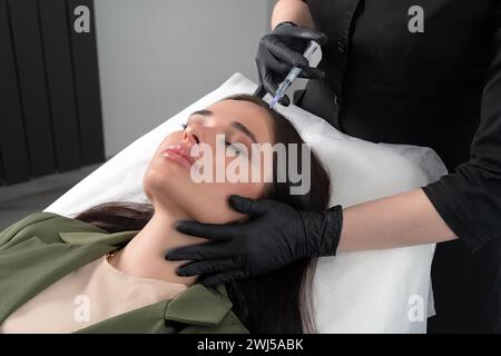 Junge Frau mit Haarproblemen, die in einer Klinik in die Kopfhaut gespritzt wird. Mesotherapeutische Behandlung des Haarausfalls, Injektion für ha Stockfoto