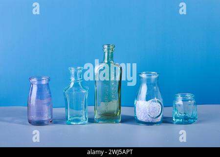 Set aus verschiedenen gedämpften farbigen Glas- und Metallflaschen und Vasen auf blauem Hintergrund. Stockfoto