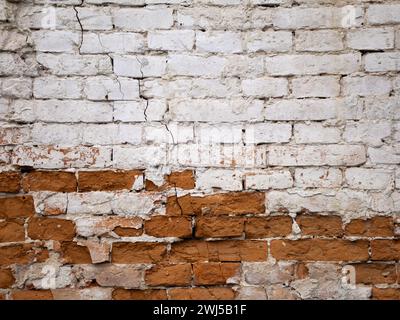 Alte Ziegelwand mit abblätternder weißer Farbe und Ziegel bröckeln durch Zeit und äußere Einflüsse Stockfoto