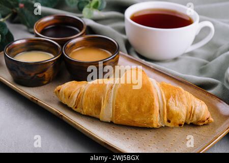 Frische französische Croissants mit Schokolade auf Teller, Heidelbeermarmelade, Honig und Tee Stockfoto