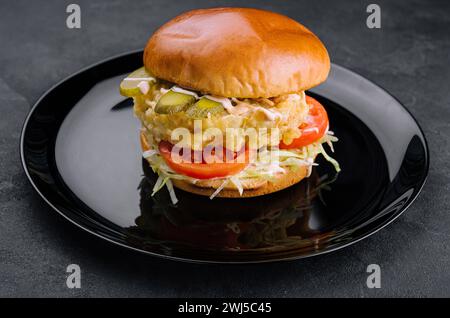 Gebratener Fisch Filet Burger auf schwarzem Teller Stockfoto