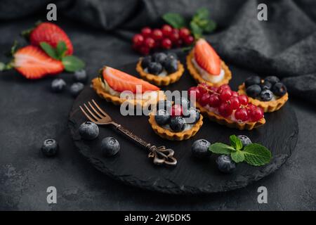Köstliche Tartlets mit Obst und Creme Mascaropne auf schwarzem Brett Stockfoto