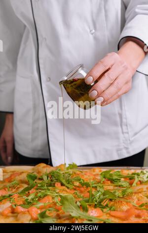 Koch gießt Olivenöl auf Pizza Stockfoto