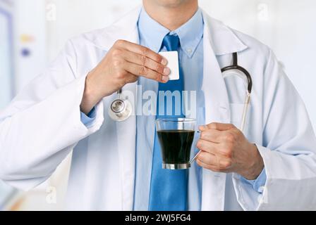 Abgeschnittener Schuss eines männlichen Arztes Hände, die Saccharin in eine Kaffeetasse im Krankenhaus werfen Stockfoto