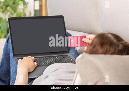 Rückansicht einer Frau, die ihre Kreditkarte verwendet, um zu Hause online zu bezahlen Stockfoto