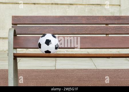 Eine einzelne Holzbank gegen eine Wand und mit einem Fußball in Verlust die Straße. Kopierraum Stockfoto