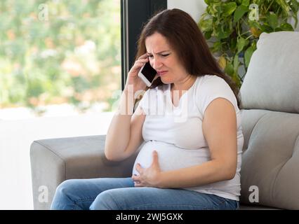 Schmerzhafte schwangere Frau, die ärztliche Hilfe ruft Stockfoto