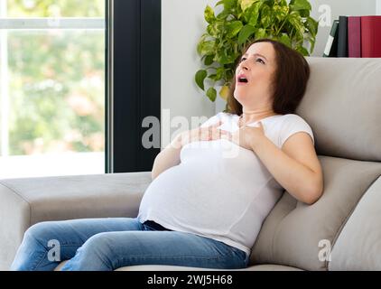 Schwangere Frau, die allein zu Hause einen Angstanfall erlitten hat Stockfoto