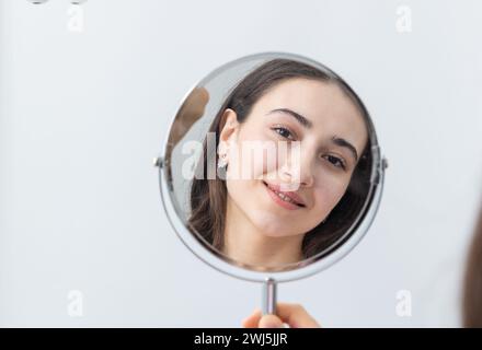 Junge Frau, die nach einem Zahnarztverfahren in den Spiegel schaut Stockfoto