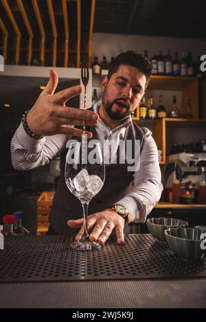 Der Barkeeper rührt Eiswürfel in einem großen Cocktailglas mit Hilfe eines Löffels an der Bar um Stockfoto