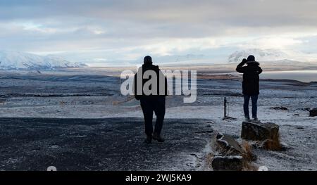 Rückansicht anonymer Touristen in warmer Kleidung, die auf verschneiten Landschaften stehen und den See und die gefrorenen Berge während der Besichtigungstour am Winterabend betrachten Stockfoto