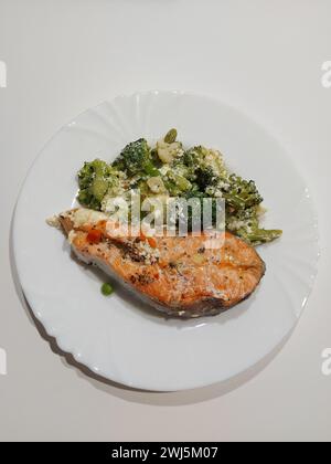 Nahaufnahme eines Stückes gegrillter Lachs mit gebackenen Brokkoli-Röschen auf einem weißen Teller auf einem weißen Tisch. Stockfoto