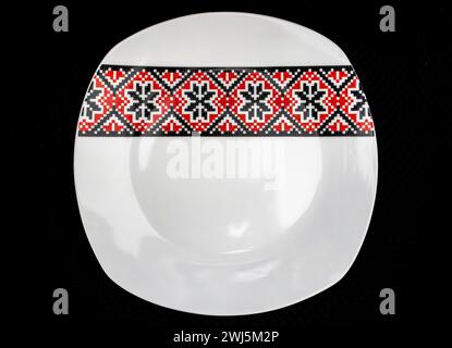 Weiße Platte mit traditionellen rumänischen Motiven in Rot und Schwarz auf schwarzem Hintergrund strahlt Eleganz und Authentizität aus. Stockfoto