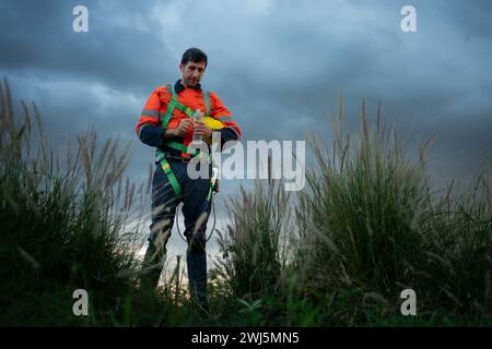 Porträt eines jungen Mannes, der auf dem Feld der Windenergieanlage arbeitet und eine Sicherheitsweste trägt, das Konzept der Entspannungszeit nach der Arbeit Stockfoto