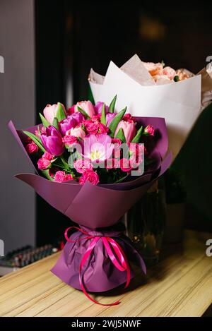 Ein exquisiter Blumenstrauß aus rosa Tulpen und Rosen, gewickelt in lila Papier mit rotem Band, perfekt für ein romantisches Geschenk oder eine Dekoration. Stockfoto