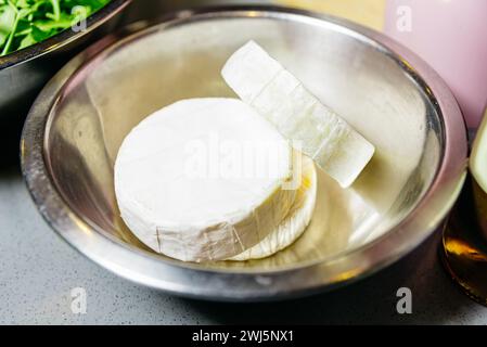 Ein ganzes Rad Brie-Käse zusammen mit einem geschnittenen Stück auf einer Metallschale, bereit für eine Gourmet-Mahlzeit oder Snack-Zubereitung. Stockfoto
