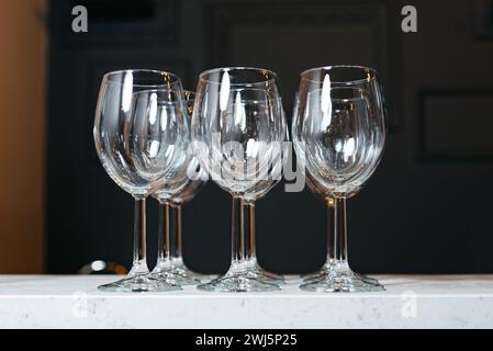Ein Satz von vier leeren Kristallweingläsern, die auf einer Arbeitsfläche aus weißem Marmor ausgestellt sind und das Licht wunderschön reflektieren. Stockfoto