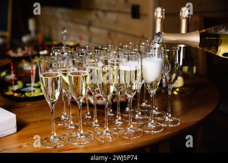 Eine Nahaufnahme des Champagners, der in Flöten gegossen wird, bereit für einen Toast bei einem privaten Ereignis mit Vorspeisen im Hintergrund. Stockfoto