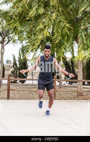 Ganzkörper eines jungen afroamerikanischen Sportlers in schwarzer Aktivkleidung, der während des Workouts im Freien an einem Seil springt Stockfoto