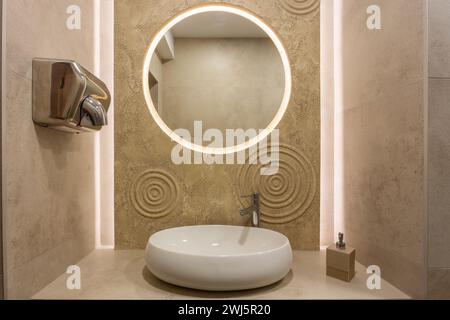 Das Innere einer öffentlichen Toilette in einem Café, Restaurant oder Bar mit Waschbecken, rundem Spiegel und Handtrockner. Stockfoto