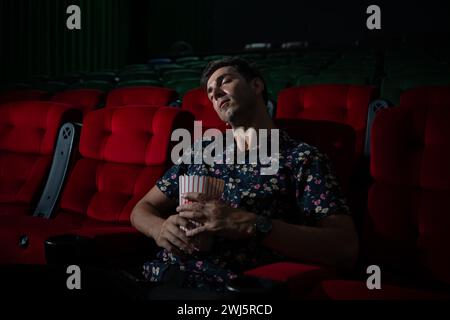 Der Mann schläft ein, während er im Kino Filme ansieht und Popcorn in der Hand, Film fehlt interessant und langweilig. Stockfoto