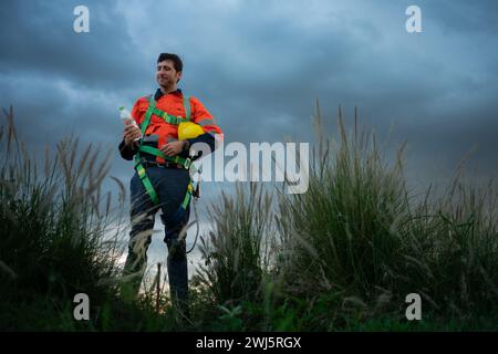 Porträt eines jungen Mannes, der auf dem Feld der Windenergieanlage arbeitet und eine Sicherheitsweste trägt, das Konzept der Entspannungszeit nach der Arbeit Stockfoto