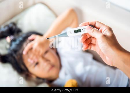 Mutter Eltern überprüfen die Temperatur ihrer kranken Tochter mit einem Digitalthermometer im Mund Stockfoto