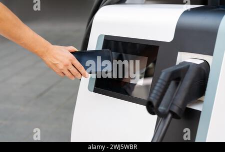 Kontaktlose mobile Bezahltechnologie an einer elektrischen Ladestation. Telefon in der Hand und mobile Ladestation. Stockfoto