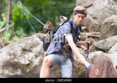 Junge Paare beim Wandern im Wald helfen einander beim Klettern, Mann und Frau beim Trekking in der Natur. Stockfoto