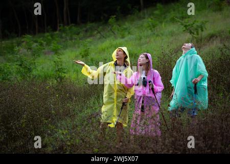 Gruppe von Freunden in Regenmänteln mit Rucksäcken auf einer Wanderung im Wald, bereiten Sie sich auf eine Wanderung vor, nachdem der Regen aufgehört hat. Stockfoto