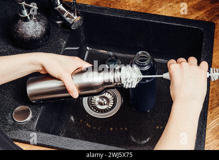 Waschreinigung wiederverwendbare Trinkwasserflasche mit Flaschenreinigungsbürste in der Wohnküche. Nachhaltiges Lifestyle-Konzept. Stockfoto