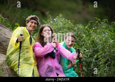 Gruppe von Freunden in Regenmänteln mit Rucksäcken auf einer Wanderung im Wald, bereiten Sie sich auf eine Wanderung vor, nachdem der Regen aufgehört hat. Stockfoto