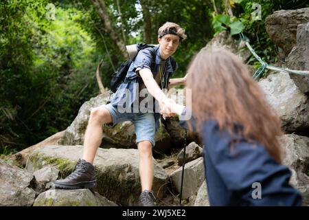 Junge Paare beim Wandern im Wald helfen einander beim Klettern, Mann und Frau beim Trekking in der Natur. Stockfoto