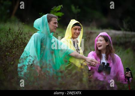 Gruppe von Freunden in Regenmänteln mit Rucksäcken auf einer Wanderung im Wald, bereiten Sie sich auf eine Wanderung vor, nachdem der Regen aufgehört hat. Stockfoto