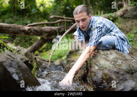 Wanderer im Dschungel, der mit Wasser in einem Bach im Wald spielt. Stockfoto